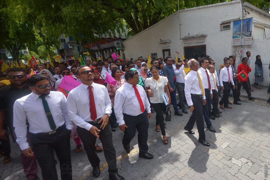 ޖުލައި 26، 2018: އިދިކޮޅު ރިޔާސީ ކެންޑިޑޭޓު އިބްރާހިމް މުހައްމަދު ސޯލިހު (އިބޫ) ގެ ކެންޑިޑެންސީ ފޯމު ހުށަހެޅުއްވުމަށް އިލެކްޝަންސް އަށް ވަޑައިގަންނަވަނީ: ގިނަ އަދަދެއްގެ ބަޔަކު އިބޫއާ އެކު އެމްޑީޕީ އޮފީހުން ފެށިގެން އިލެކްޝަންސް ކޮމިޝަނުގެ އިދާރާއަށް ގޮސްފައިވަނީ ބެރު ޖަހަމުން ހިނގާފައި  --- ސަންފޮޓޯ/ މުހައްމަދު އަފްރާހް
