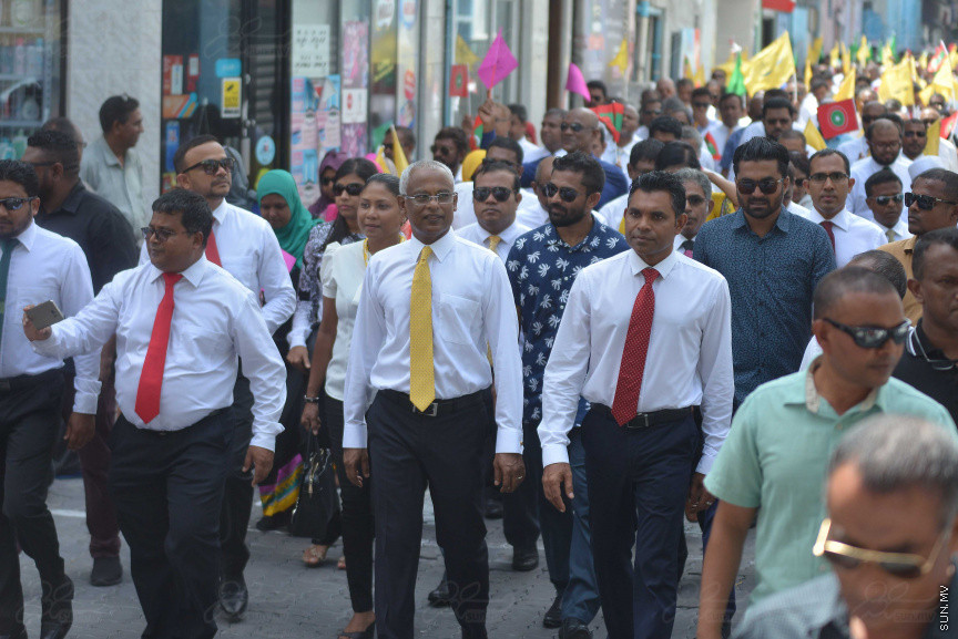 ޖުލައި 26، 2018: އިދިކޮޅު ރިޔާސީ ކެންޑިޑޭޓު އިބްރާހިމް މުހައްމަދު ސޯލިހު (އިބޫ) ގެ ކެންޑިޑެންސީ ފޯމު ހުށަހެޅުއްވުމަށް އިލެކްޝަންސް އަށް ވަޑައިގަންނަވަނީ: ގިނަ އަދަދެއްގެ ބަޔަކު އިބޫއާ އެކު އެމްޑީޕީ އޮފީހުން ފެށިގެން އިލެކްޝަންސް ކޮމިޝަނުގެ އިދާރާއަށް ގޮސްފައިވަނީ ބެރު ޖަހަމުން ހިނގާފައި  --- ސަންފޮޓޯ/ މުހައްމަދު އަފްރާހް