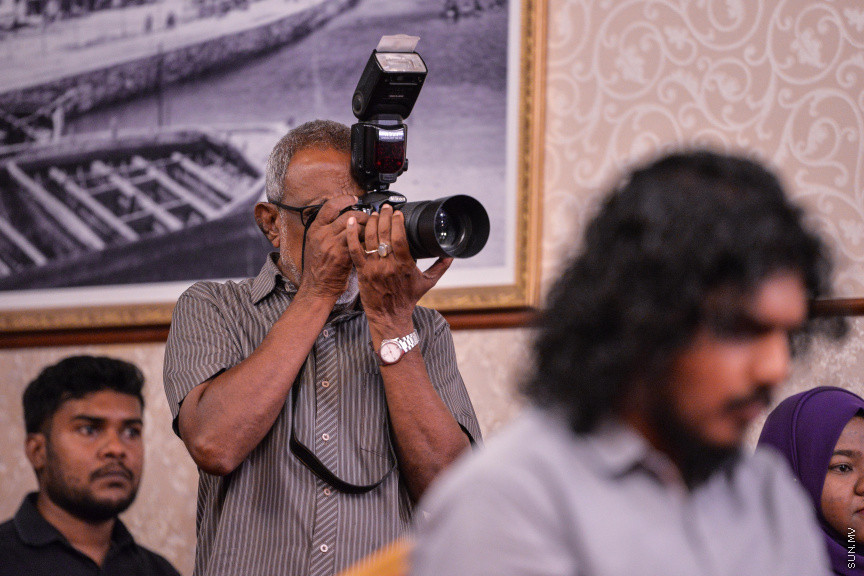 މާޗް 27، 2020: ކޮވިޑް19ގެ ނުރައްކާ ރާއްޖެއަށް ބޮޑުވެ، މުޅި ރާއްޖޭގައި ސިއްހީ ކުއްލި ނުރައްކާ އިއުލާން ކުރީ މި މަހުގެ 12 ވަނަ ދުވަހުއެވެ. އޭގެ ކުރިން ވެސް ކޮވިޑް19ގެ ހާލަތު އޮތް މިންވަރު ސަރުކާރުން ދިޔައީ ބުނެދެމުންނެވެ. ކޮވިޑް-19ގެ ތަރުޖާމާނެއްގެ ގޮތުގުގައި ރައީސް އޮފީހުގެ އަންޑަ ސެކްރެޓަރީ މަބްރޫކް އަބްދުލް އަޒީޒް ކަނޑައެޅުމާ އެކު ކޮންމެ ދުވަހަކު އެ ބޭފުޅާ ގެންދަވަނީ މީޑިއާތަކަށް މައުލޫމާތު ދެއްވަމުންނެވެ. ހުކުރު ދުވަސް ފިޔަވައި ކޮންމެ ދުވަަކު ދެ އިރު ޕްރެސް ކޮންފަރެންސް ދެއްވައެވެ. ހުކުރު ދުވަހުގެ ރޭ ވެސް ޕްރެސް ދެއްވައެވެ. ސަރުކާރު ބަންދުކޮށް، ކެފޭތަކާއި ރެސްޓޯރަންތުތައް ބަންދުކޮށްފައިވުމުން، ގޭގައި ތިބެގެން ގިނަ ބަޔަކު މަބްރޫކް ބާއްވާ ޕްރެސް ކޮންފަރެންސްތައް ދަނީ ބަލަމުންނެވެ. މި ފޮޓޯތަކުން މި ފެންނަނީ އެ ޕްރެސް ކޮންފަރެންސްތަކުގެ އަނެއް ފަރާތެވެ -- ސަން ފޮޓޯ/ ފަޔާޒު މޫސާ