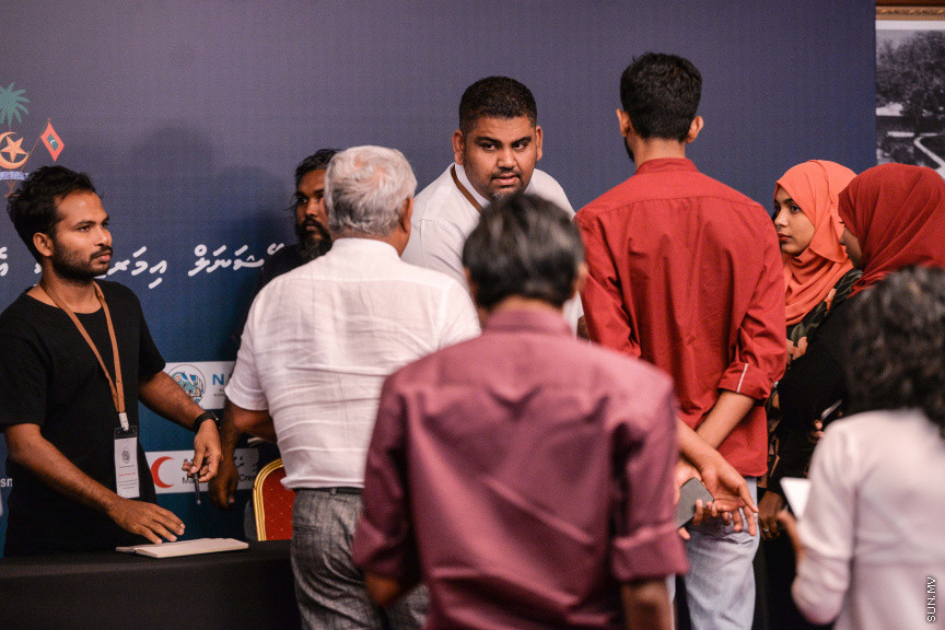މާޗް 27، 2020: ކޮވިޑް19ގެ ނުރައްކާ ރާއްޖެއަށް ބޮޑުވެ، މުޅި ރާއްޖޭގައި ސިއްހީ ކުއްލި ނުރައްކާ އިއުލާން ކުރީ މި މަހުގެ 12 ވަނަ ދުވަހުއެވެ. އޭގެ ކުރިން ވެސް ކޮވިޑް19ގެ ހާލަތު އޮތް މިންވަރު ސަރުކާރުން ދިޔައީ ބުނެދެމުންނެވެ. ކޮވިޑް-19ގެ ތަރުޖާމާނެއްގެ ގޮތުގުގައި ރައީސް އޮފީހުގެ އަންޑަ ސެކްރެޓަރީ މަބްރޫކް އަބްދުލް އަޒީޒް ކަނޑައެޅުމާ އެކު ކޮންމެ ދުވަހަކު އެ ބޭފުޅާ ގެންދަވަނީ މީޑިއާތަކަށް މައުލޫމާތު ދެއްވަމުންނެވެ. ހުކުރު ދުވަސް ފިޔަވައި ކޮންމެ ދުވަަކު ދެ އިރު ޕްރެސް ކޮންފަރެންސް ދެއްވައެވެ. ހުކުރު ދުވަހުގެ ރޭ ވެސް ޕްރެސް ދެއްވައެވެ. ސަރުކާރު ބަންދުކޮށް، ކެފޭތަކާއި ރެސްޓޯރަންތުތައް ބަންދުކޮށްފައިވުމުން، ގޭގައި ތިބެގެން ގިނަ ބަޔަކު މަބްރޫކް ބާއްވާ ޕްރެސް ކޮންފަރެންސްތައް ދަނީ ބަލަމުންނެވެ. މި ފޮޓޯތަކުން މި ފެންނަނީ އެ ޕްރެސް ކޮންފަރެންސްތަކުގެ އަނެއް ފަރާތެވެ -- ސަން ފޮޓޯ/ ފަޔާޒު މޫސާ